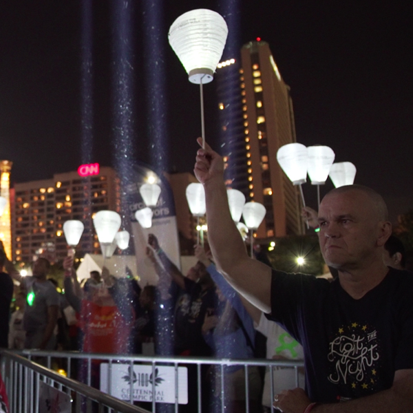 Cancer survivors holding up white lanterns symbolizing, surviving cancer.